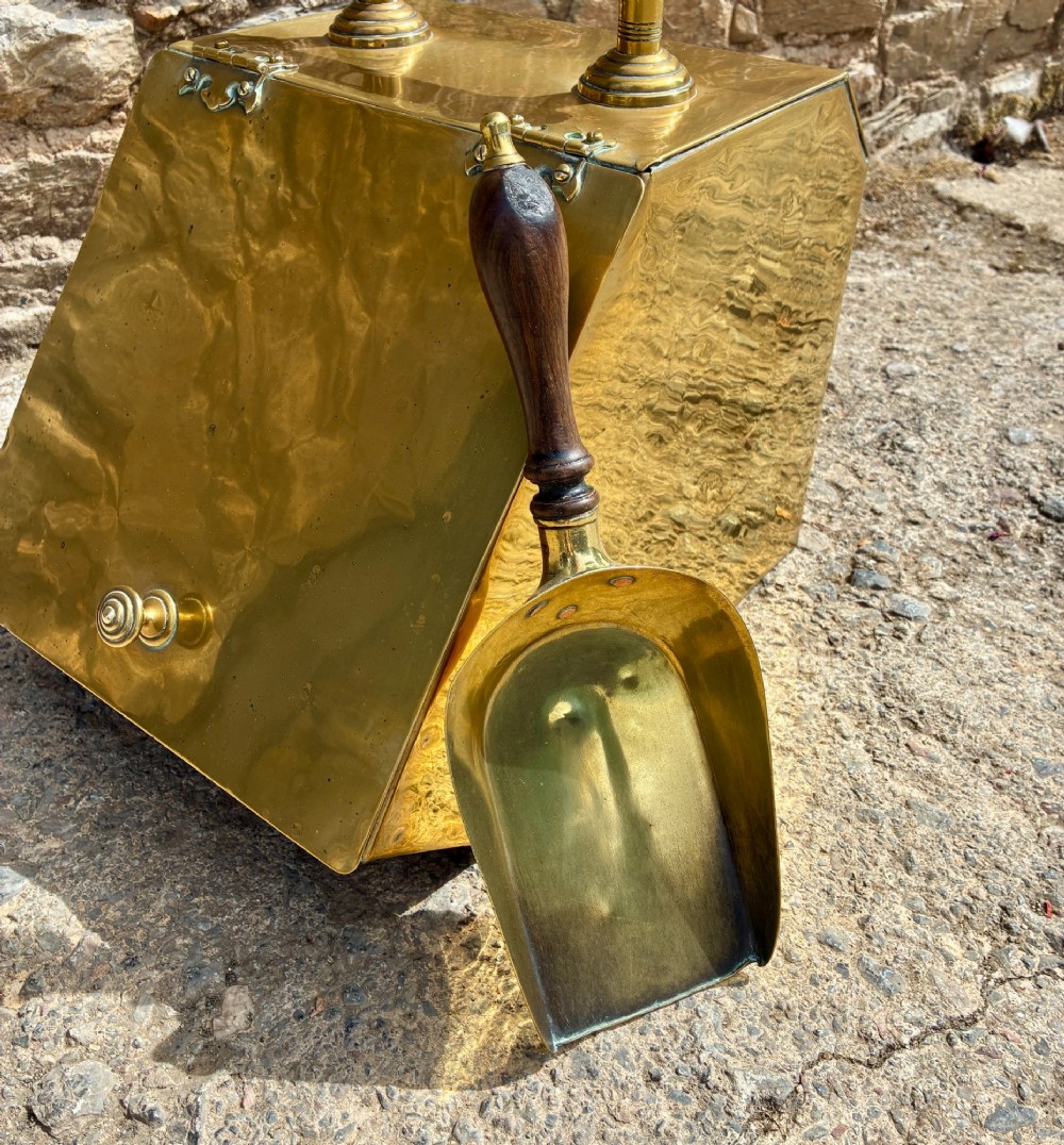 An antique brass sloped coal scuttle featuring a turned wooden carrying handle, a hinged lid, and an attached brass shovel at the rear. View XIV