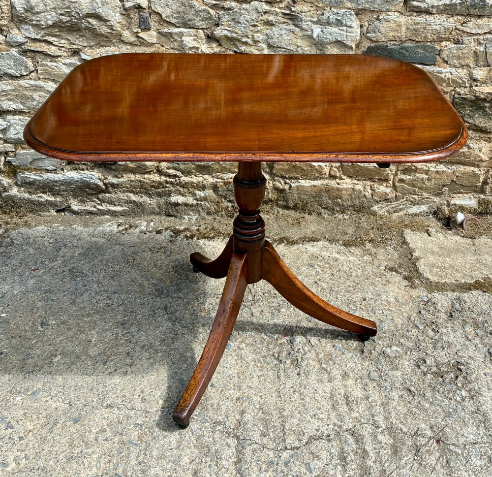 A Victorian mahogany tilt-top table featuring a polished rounded rectangular surface set on a turned pedestal column with three splayed legs.