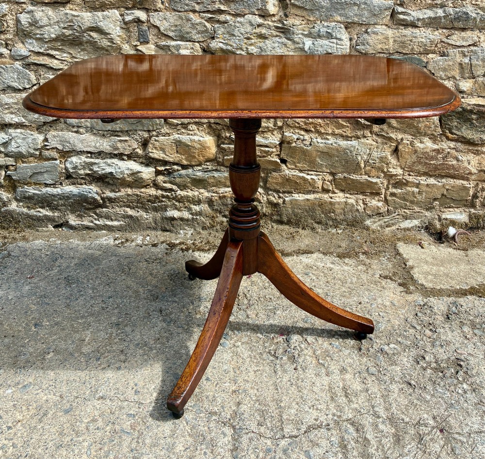 A Victorian mahogany tilt-top table featuring a polished rounded rectangular surface set on a turned pedestal column with three splayed legs. View II