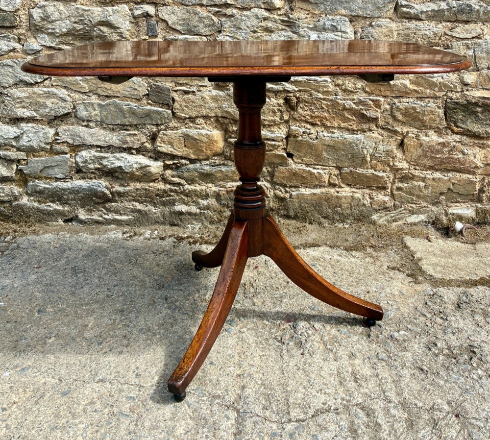 A Victorian mahogany tilt-top table featuring a polished rounded rectangular surface set on a turned pedestal column with three splayed legs. View V