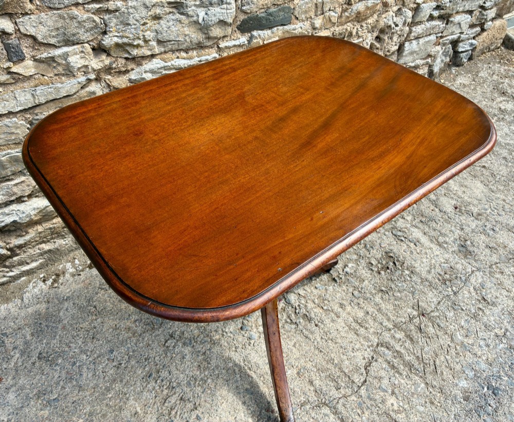A Victorian mahogany tilt-top table featuring a polished rounded rectangular surface set on a turned pedestal column with three splayed legs. View VI