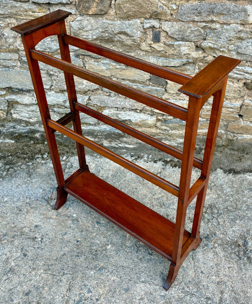 An Edwardian mahogany freestanding towel rail featuring double horizontal bars, a lower solid wooden shelf, vertical side supports, and flared feet. View II
