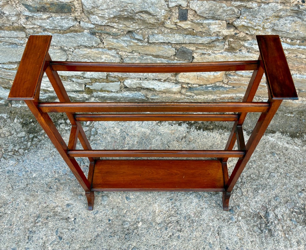 An Edwardian mahogany freestanding towel rail featuring double horizontal bars, a lower solid wooden shelf, vertical side supports, and flared feet. View VII