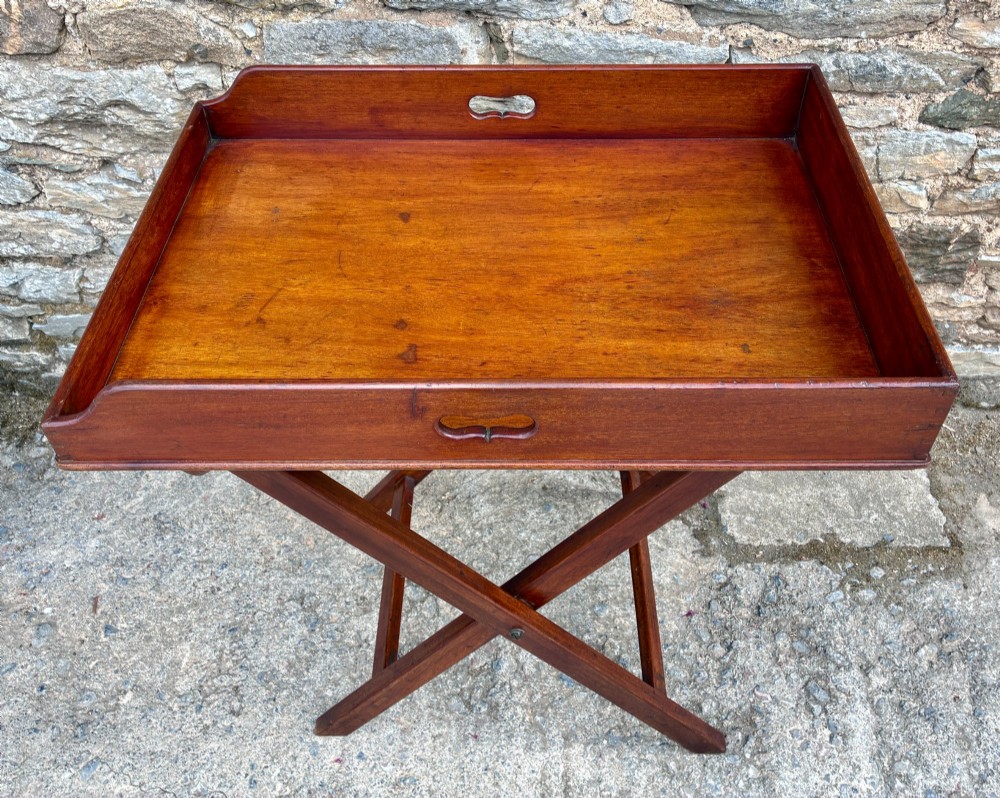 A Victorian mahogany butlers tray with cut-out hand holes resting on a folding wooden X-frame stand. View II