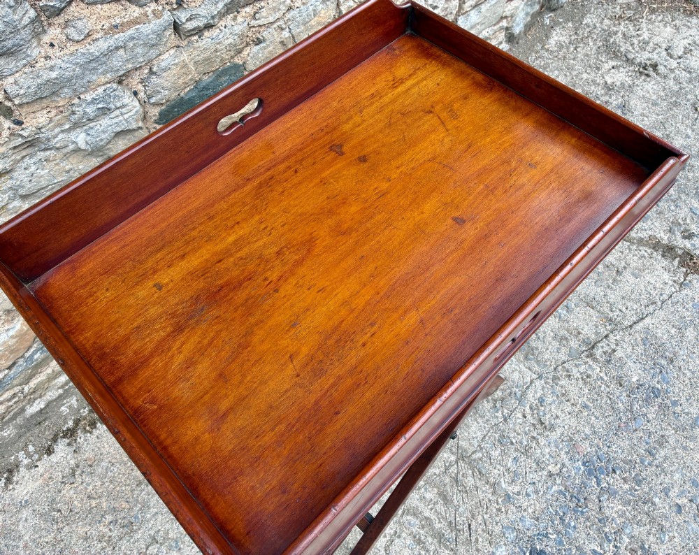 A Victorian mahogany butlers tray with cut-out hand holes resting on a folding wooden X-frame stand. View VIII