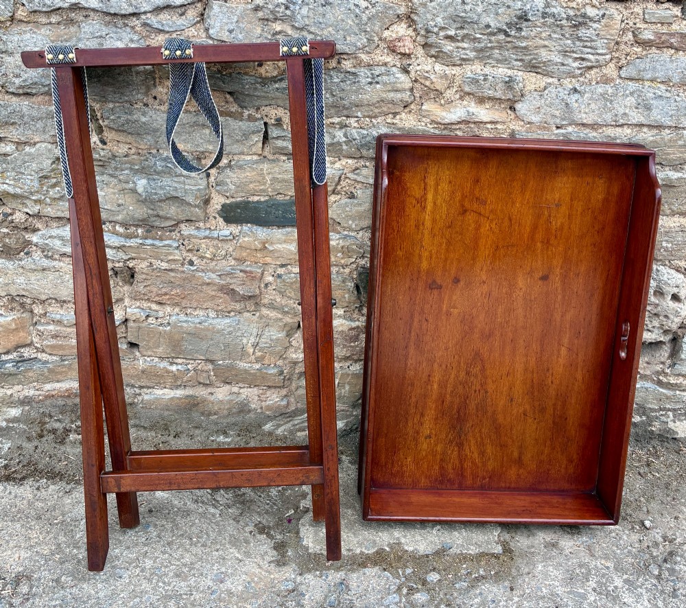 A Victorian mahogany butlers tray with cut-out hand holes resting on a folding wooden X-frame stand. View X