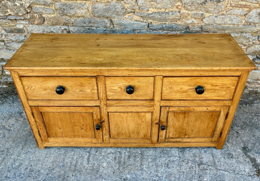 A nineteenth-century pine dresser base featuring three top drawers, three lower panelled cupboard doors, and turned dark wooden knobs. View II