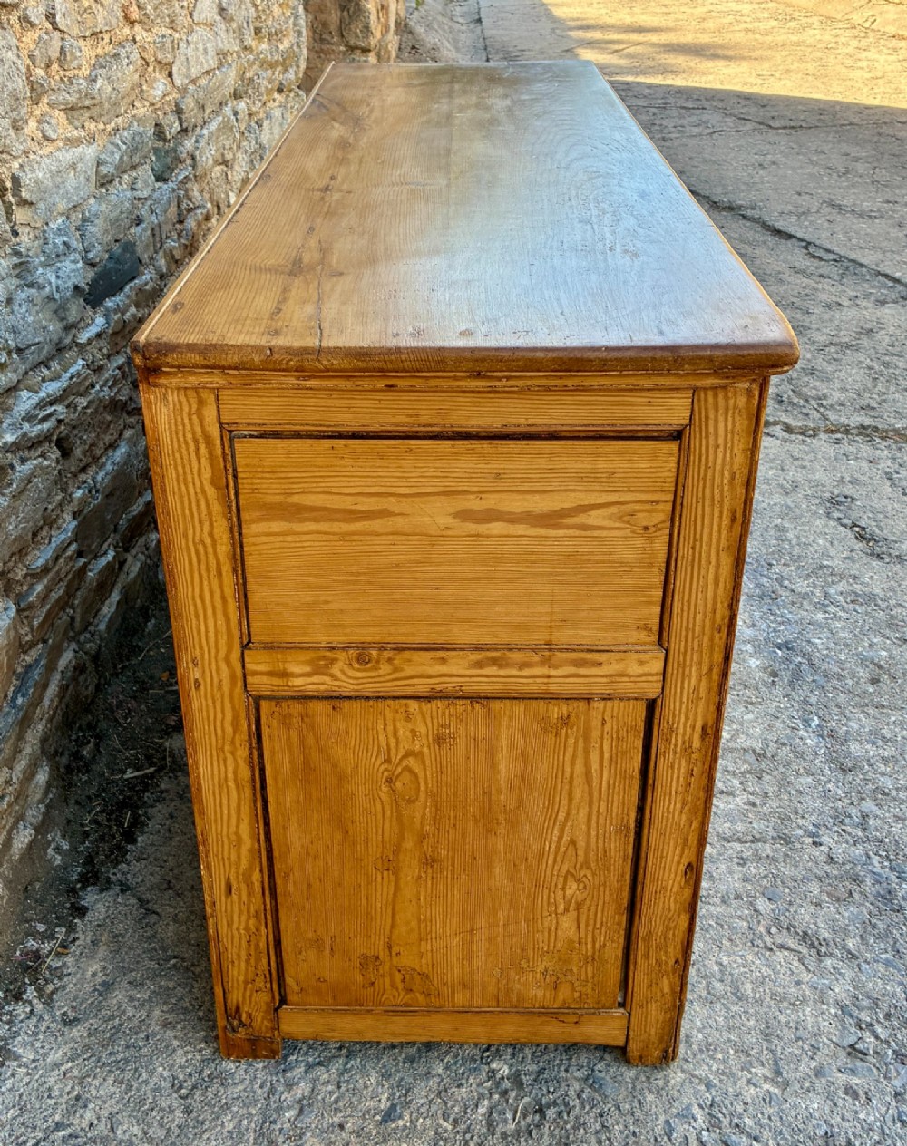 A nineteenth-century pine dresser base featuring three top drawers, three lower panelled cupboard doors, and turned dark wooden knobs. View V
