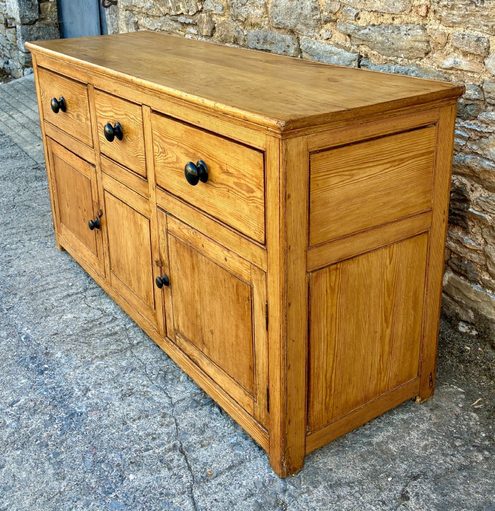 A nineteenth-century pine dresser base featuring three top drawers, three lower panelled cupboard doors, and turned dark wooden knobs. View VI