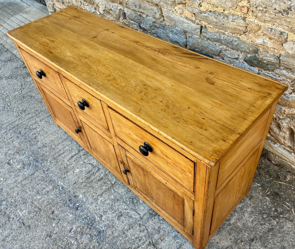 A nineteenth-century pine dresser base featuring three top drawers, three lower panelled cupboard doors, and turned dark wooden knobs. View VIII
