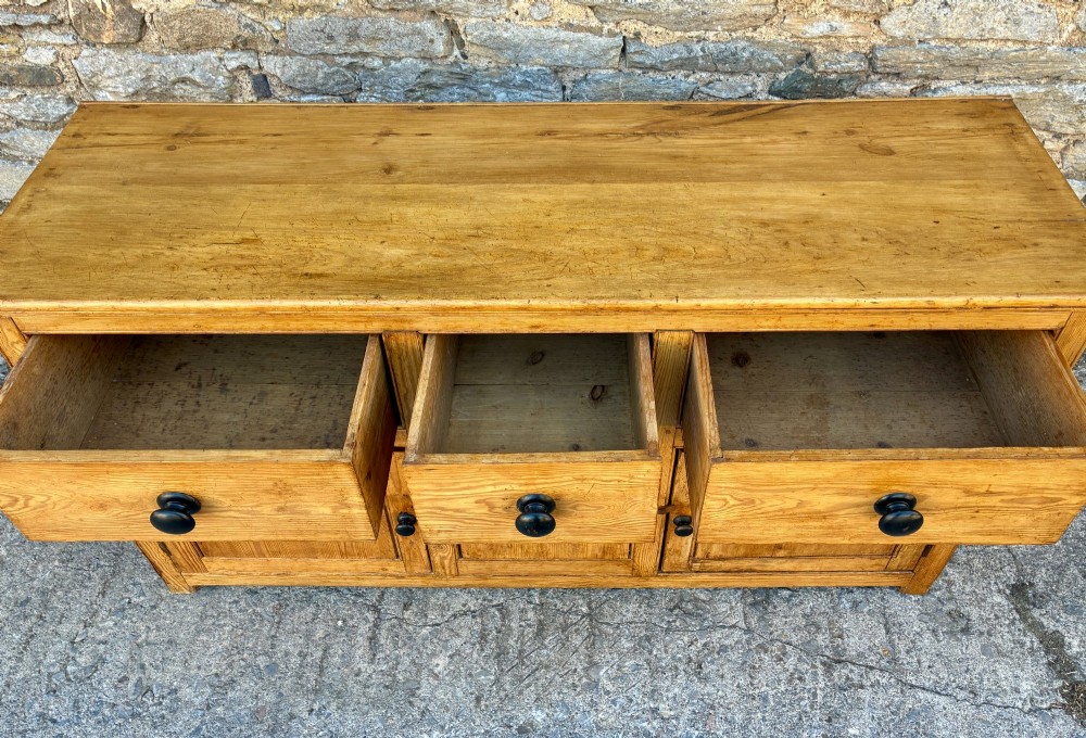 A nineteenth-century pine dresser base featuring three top drawers, three lower panelled cupboard doors, and turned dark wooden knobs. View IX