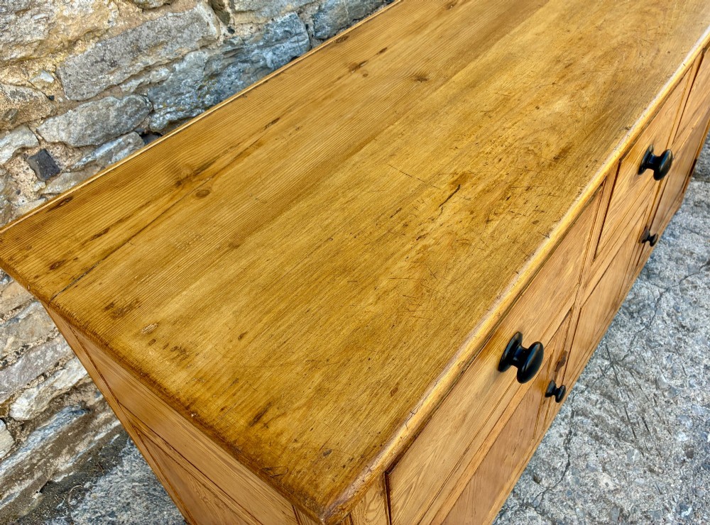 A nineteenth-century pine dresser base featuring three top drawers, three lower panelled cupboard doors, and turned dark wooden knobs. View X