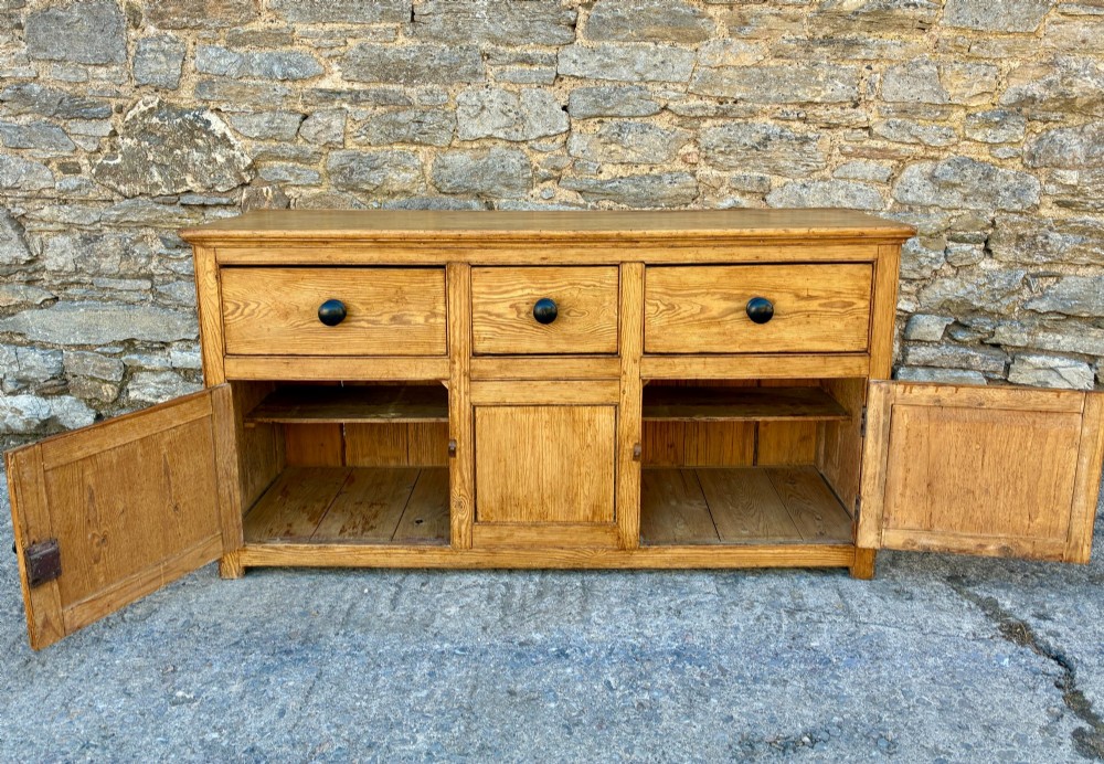 A nineteenth-century pine dresser base featuring three top drawers, three lower panelled cupboard doors, and turned dark wooden knobs. View XI