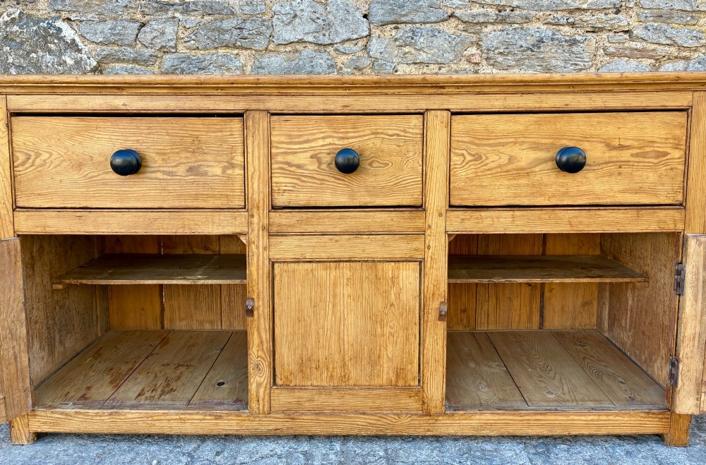 A nineteenth-century pine dresser base featuring three top drawers, three lower panelled cupboard doors, and turned dark wooden knobs. View XII