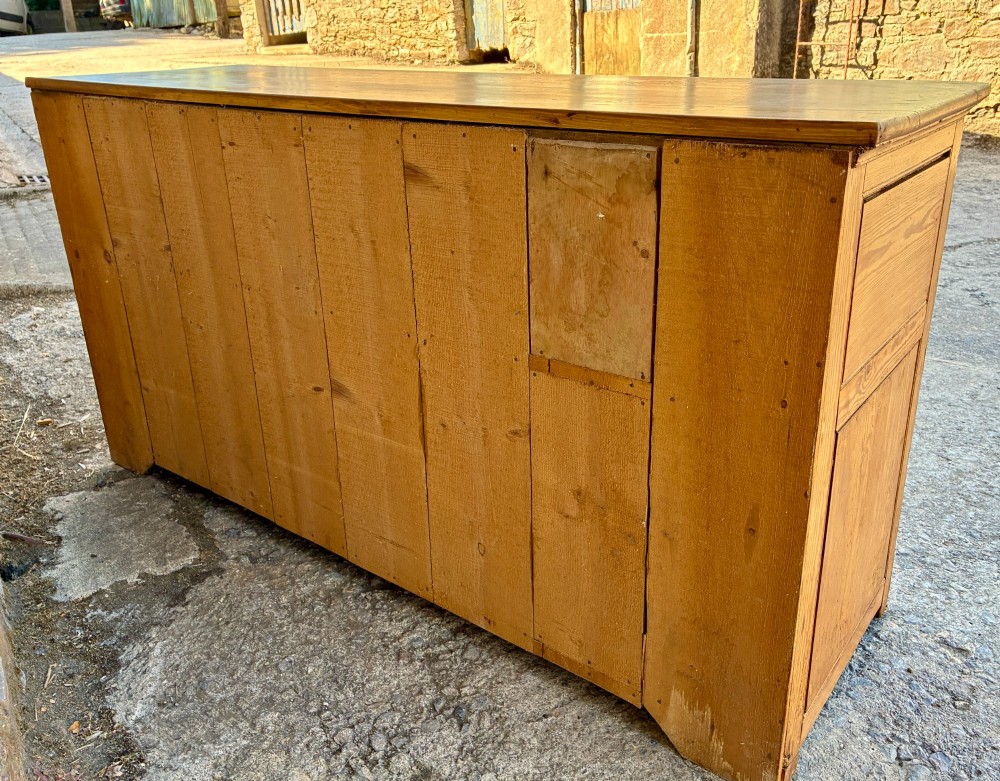 A nineteenth-century pine dresser base featuring three top drawers, three lower panelled cupboard doors, and turned dark wooden knobs. View XV