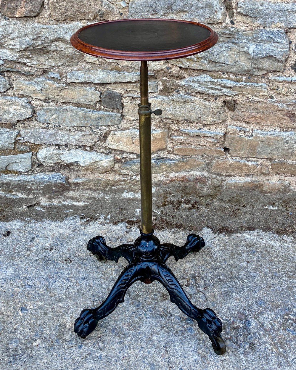 Victorian adjustable display stand featuring a round mahogany top, a brass telescoping stem, and a black cast iron paw-foot base.
