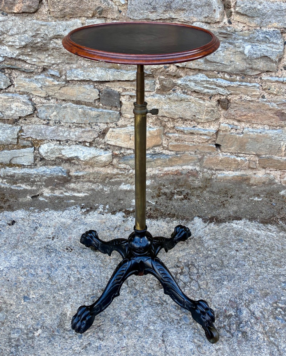 Victorian adjustable display stand featuring a round mahogany top, a brass telescoping stem, and a black cast iron paw-foot base. View X