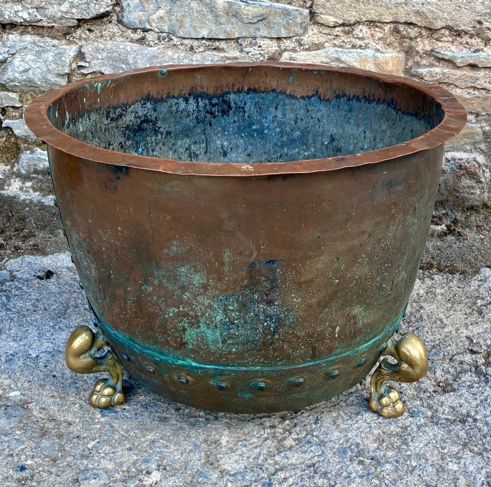 A large round copper boiler with a hand-riveted base seam and flared rim, supported on four decorative cast brass claw feet.