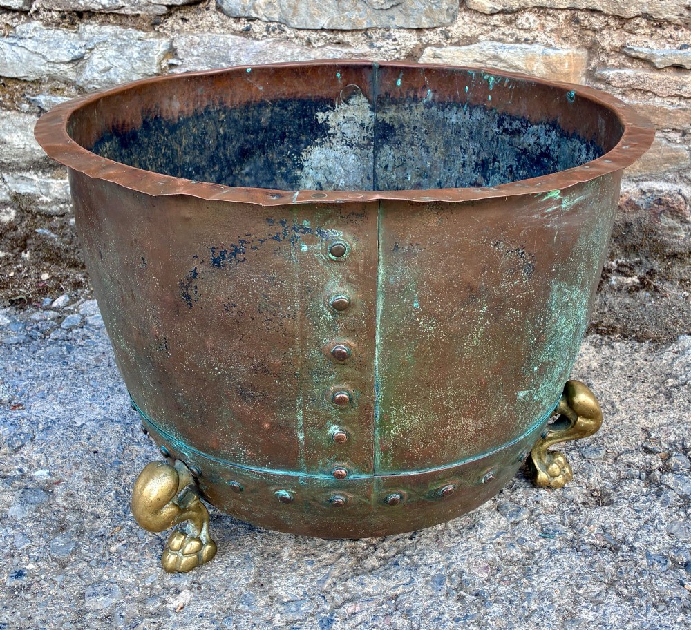 A large round copper boiler with a hand-riveted base seam and flared rim, supported on four decorative cast brass claw feet. View IV
