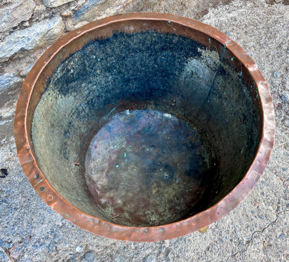A large round copper boiler with a hand-riveted base seam and flared rim, supported on four decorative cast brass claw feet. View VI