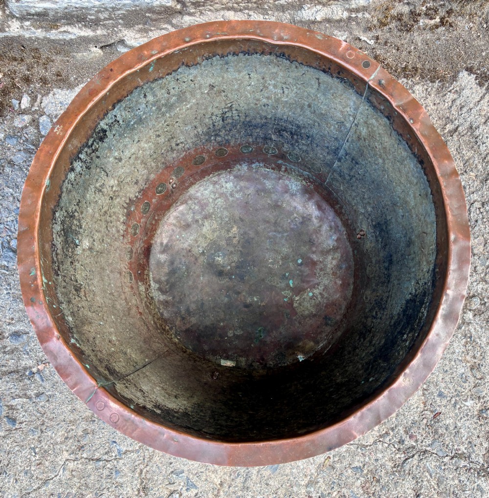 A large round copper boiler with a hand-riveted base seam and flared rim, supported on four decorative cast brass claw feet. View IX