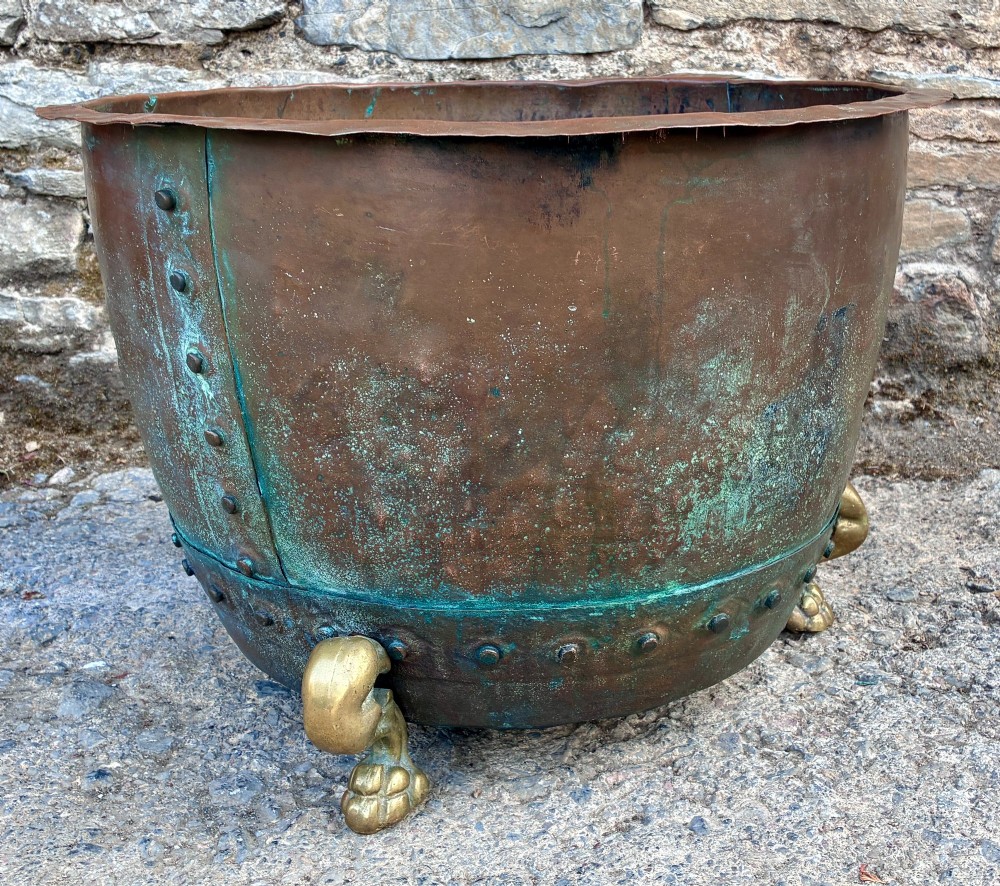 A large round copper boiler with a hand-riveted base seam and flared rim, supported on four decorative cast brass claw feet. View X
