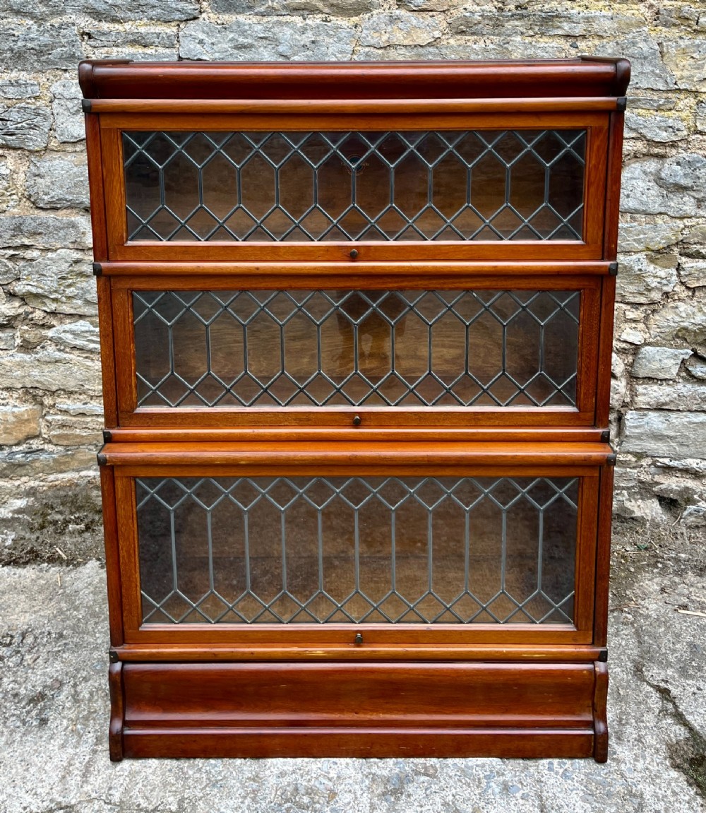 A three-tier Globe Wernicke mahogany barristers bookcase featuring leaded glass lift-up doors and a moulded plinth base.
