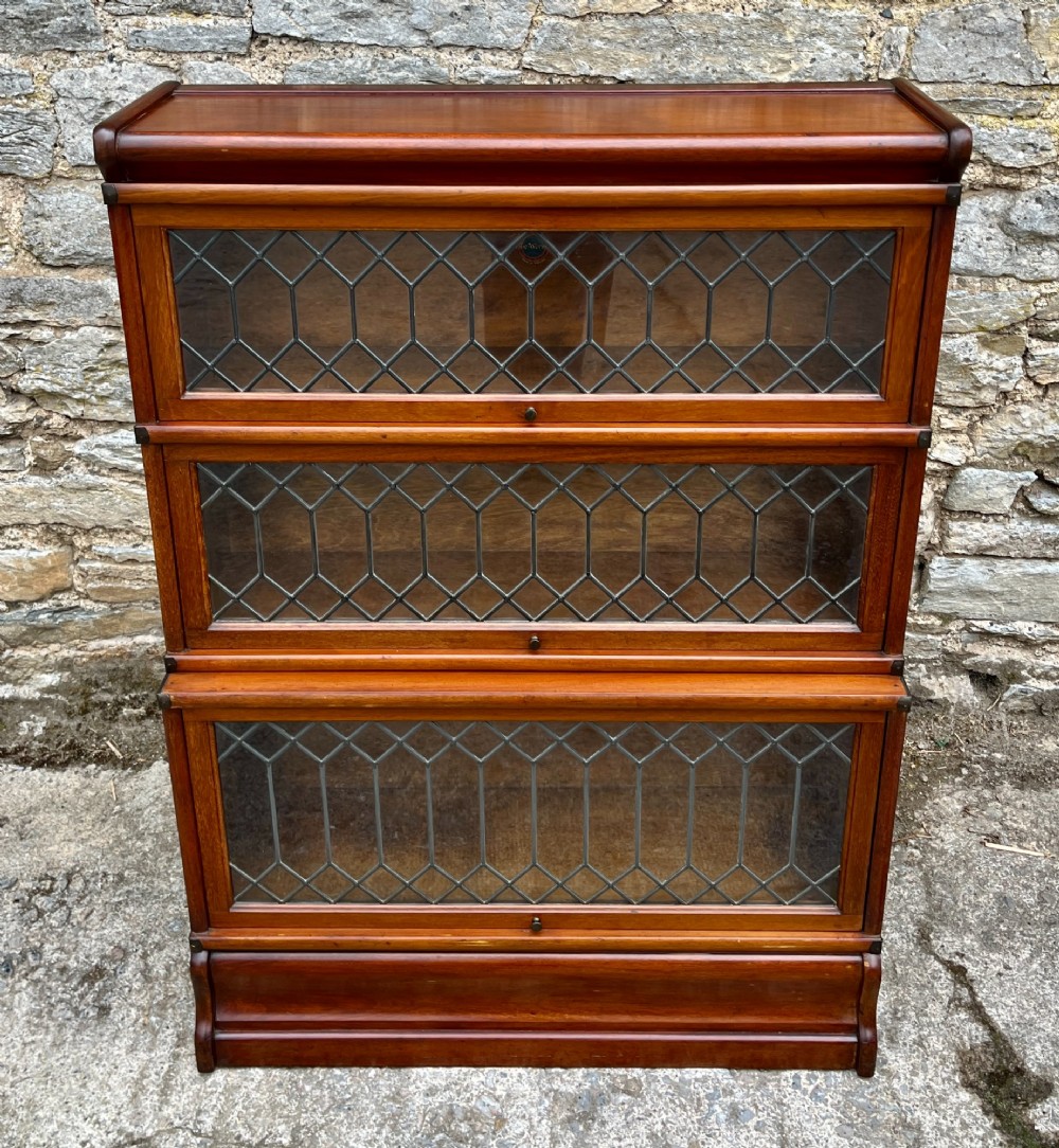 A three-tier Globe Wernicke mahogany barristers bookcase featuring leaded glass lift-up doors and a moulded plinth base. View II