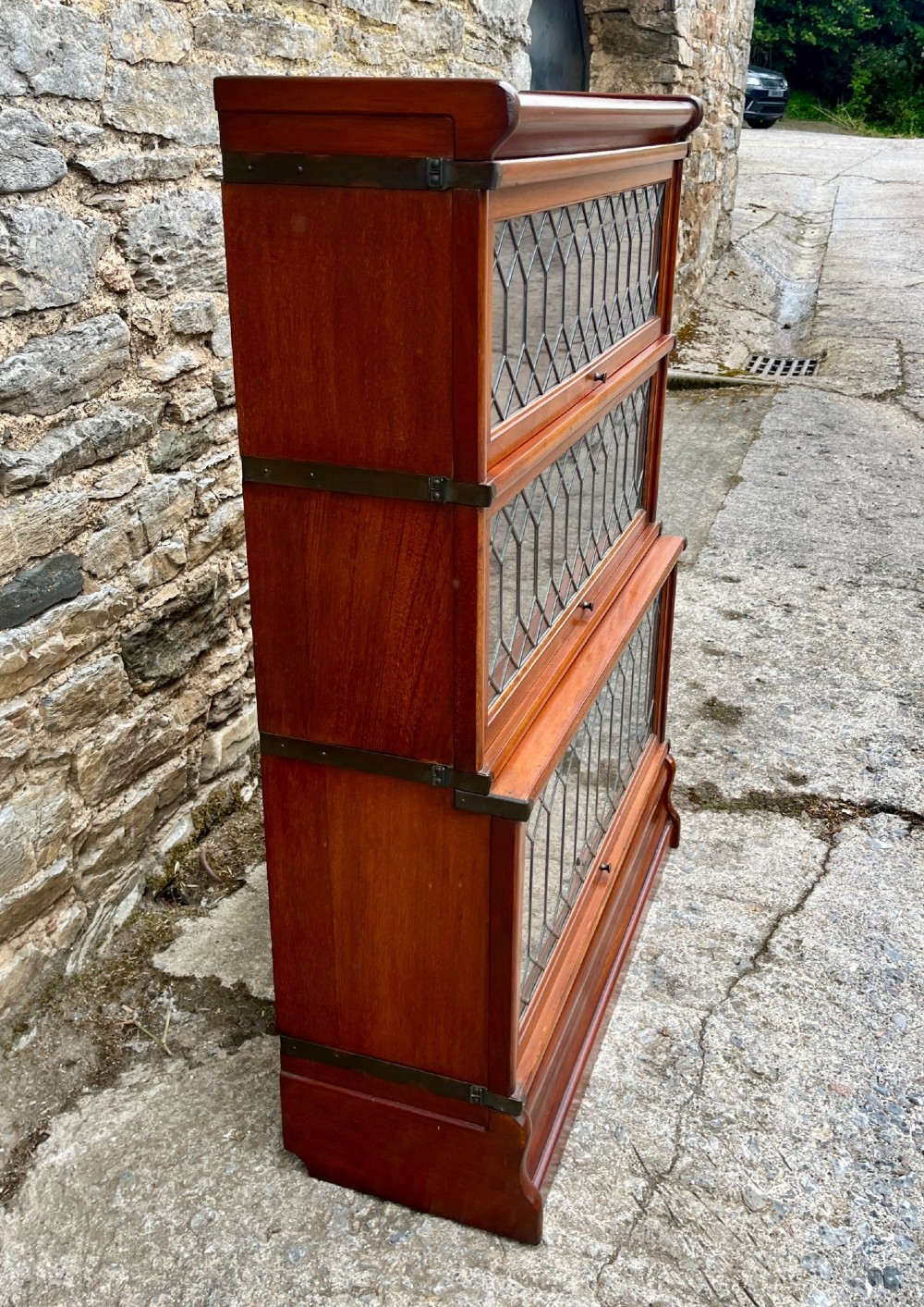 A three-tier Globe Wernicke mahogany barristers bookcase featuring leaded glass lift-up doors and a moulded plinth base. View IV