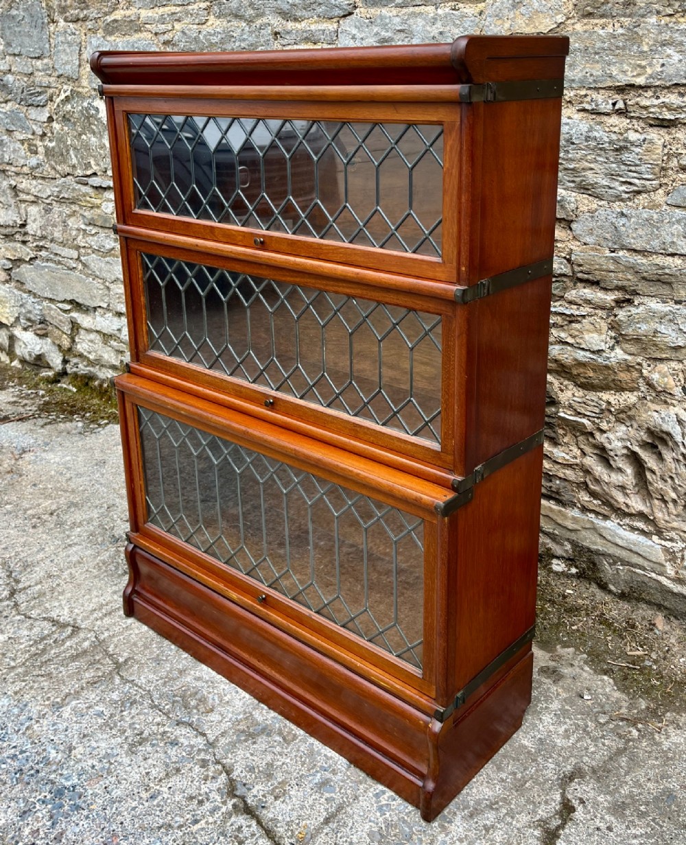 A three-tier Globe Wernicke mahogany barristers bookcase featuring leaded glass lift-up doors and a moulded plinth base. View V