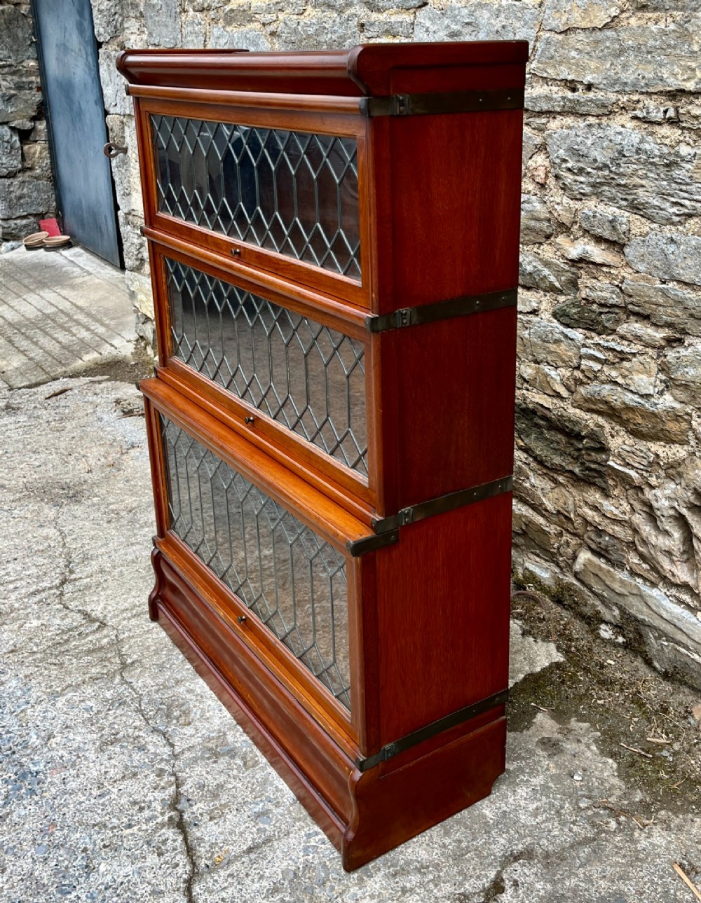 A three-tier Globe Wernicke mahogany barristers bookcase featuring leaded glass lift-up doors and a moulded plinth base. View VI