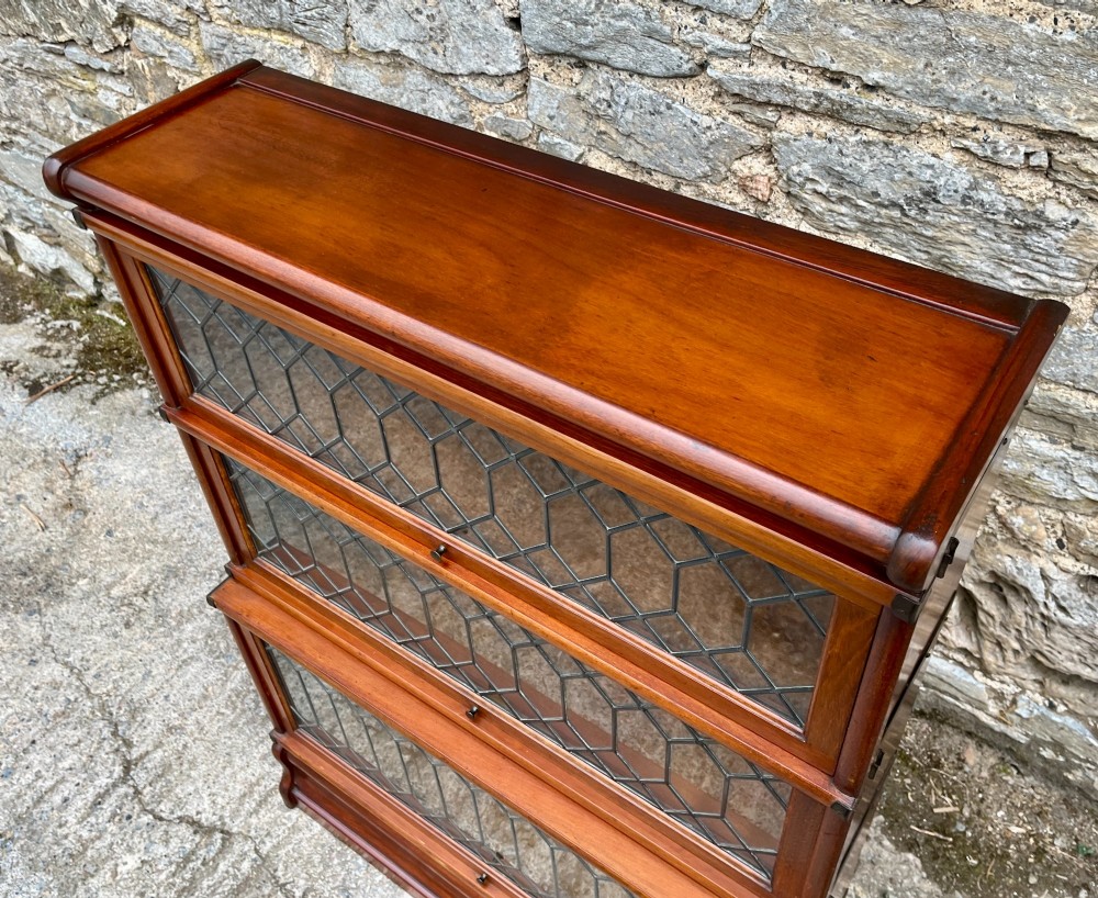 A three-tier Globe Wernicke mahogany barristers bookcase featuring leaded glass lift-up doors and a moulded plinth base. View VII