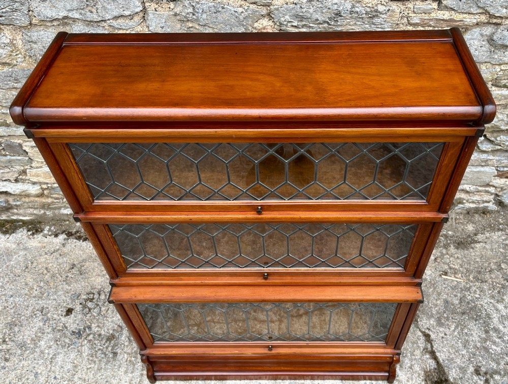 A three-tier Globe Wernicke mahogany barristers bookcase featuring leaded glass lift-up doors and a moulded plinth base. View VIII