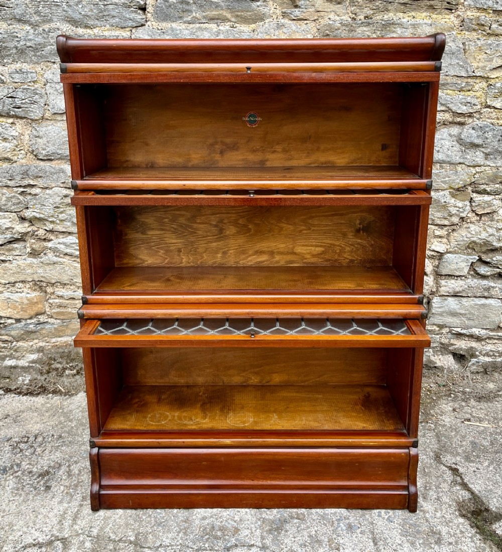 A three-tier Globe Wernicke mahogany barristers bookcase featuring leaded glass lift-up doors and a moulded plinth base. View X