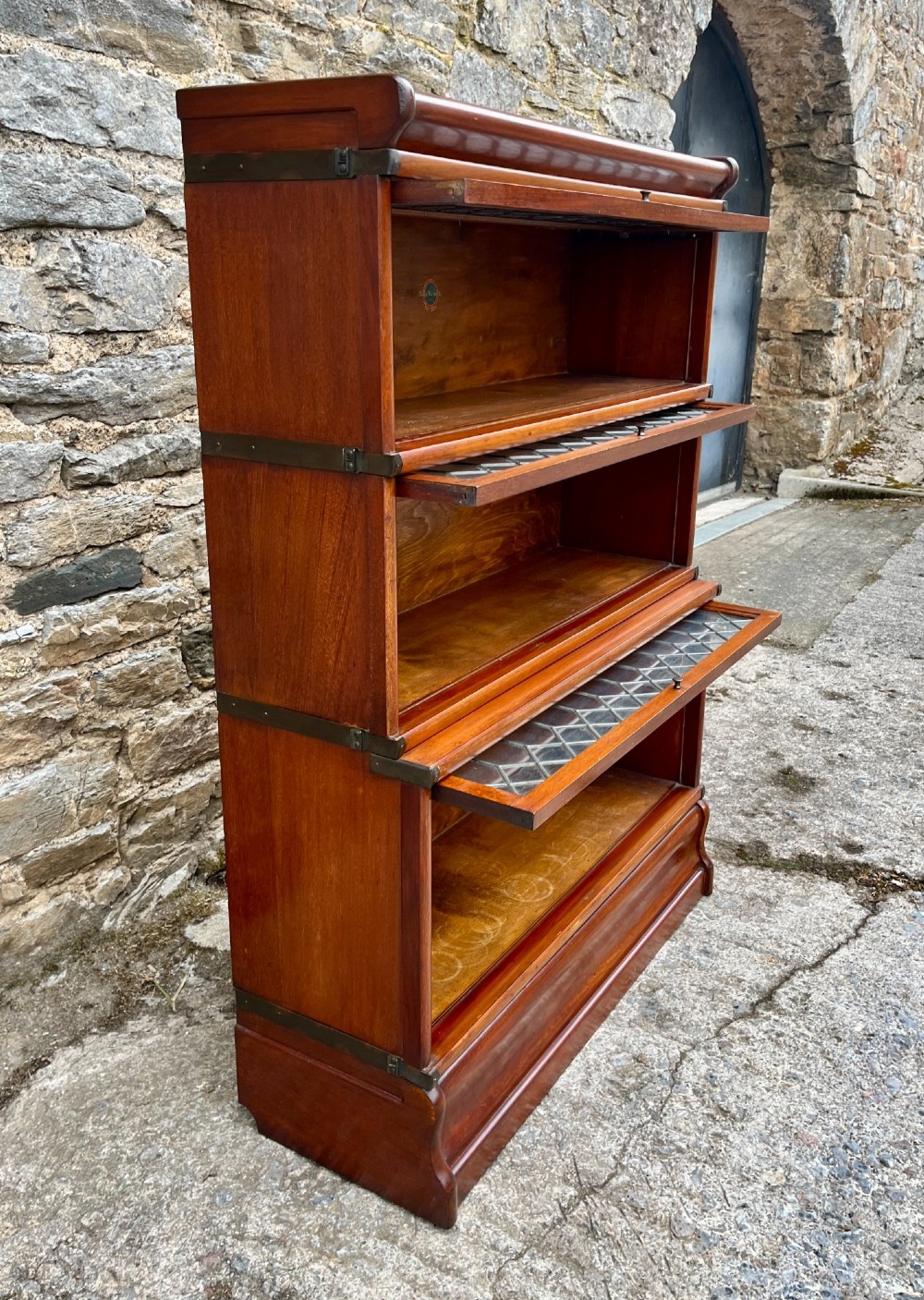 A three-tier Globe Wernicke mahogany barristers bookcase featuring leaded glass lift-up doors and a moulded plinth base. View XI