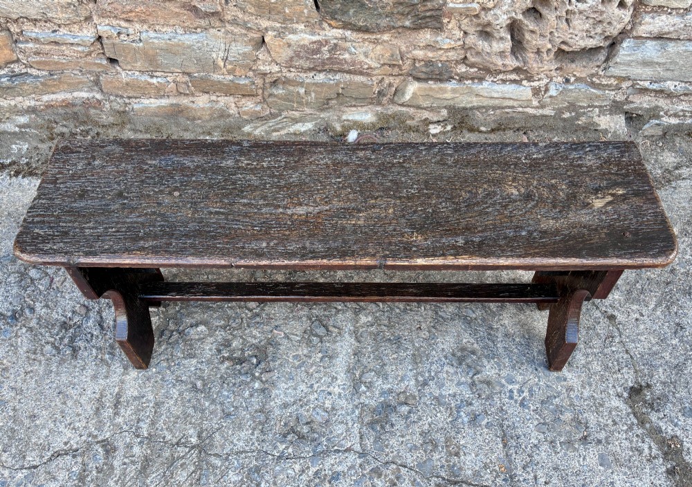 A long antique dark wooden hall bench featuring a flat plank seat, shaped slab end supports, and a lower wooden stretcher. View II