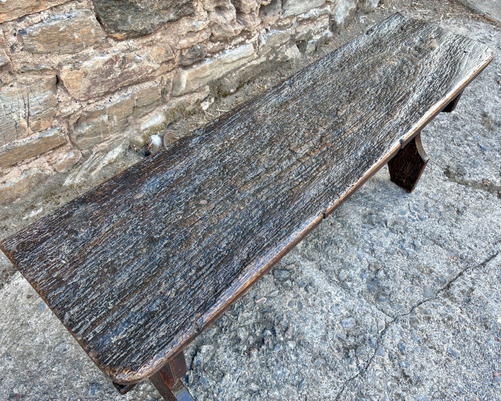 A long antique dark wooden hall bench featuring a flat plank seat, shaped slab end supports, and a lower wooden stretcher. View III