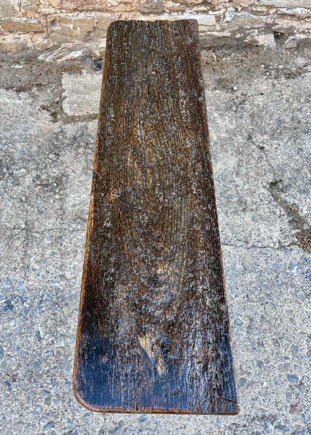 A long antique dark wooden hall bench featuring a flat plank seat, shaped slab end supports, and a lower wooden stretcher. View VI