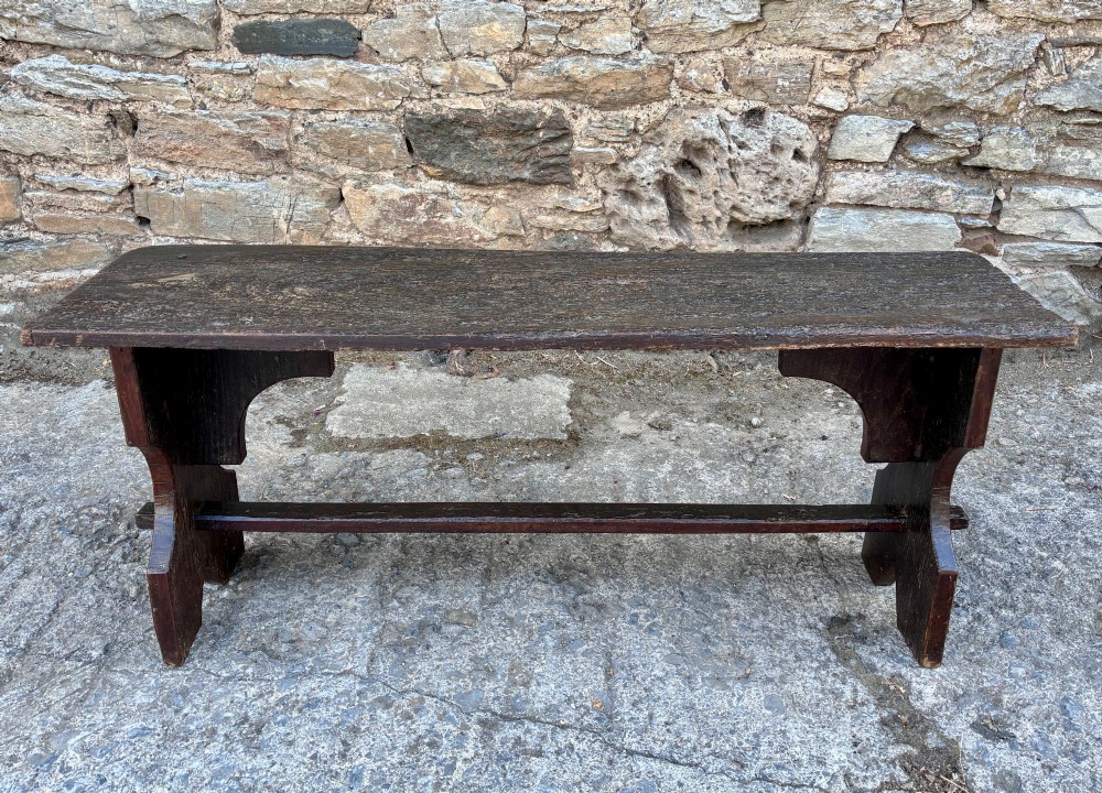 A long antique dark wooden hall bench featuring a flat plank seat, shaped slab end supports, and a lower wooden stretcher. View VII