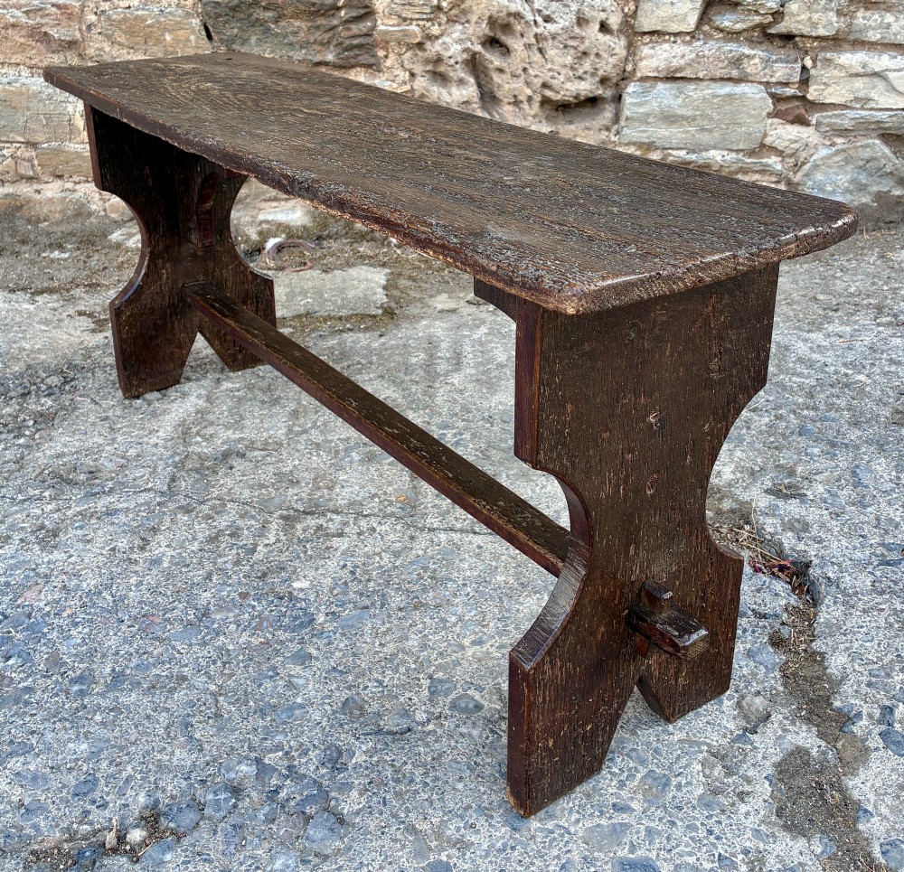 A long antique dark wooden hall bench featuring a flat plank seat, shaped slab end supports, and a lower wooden stretcher. View VIII