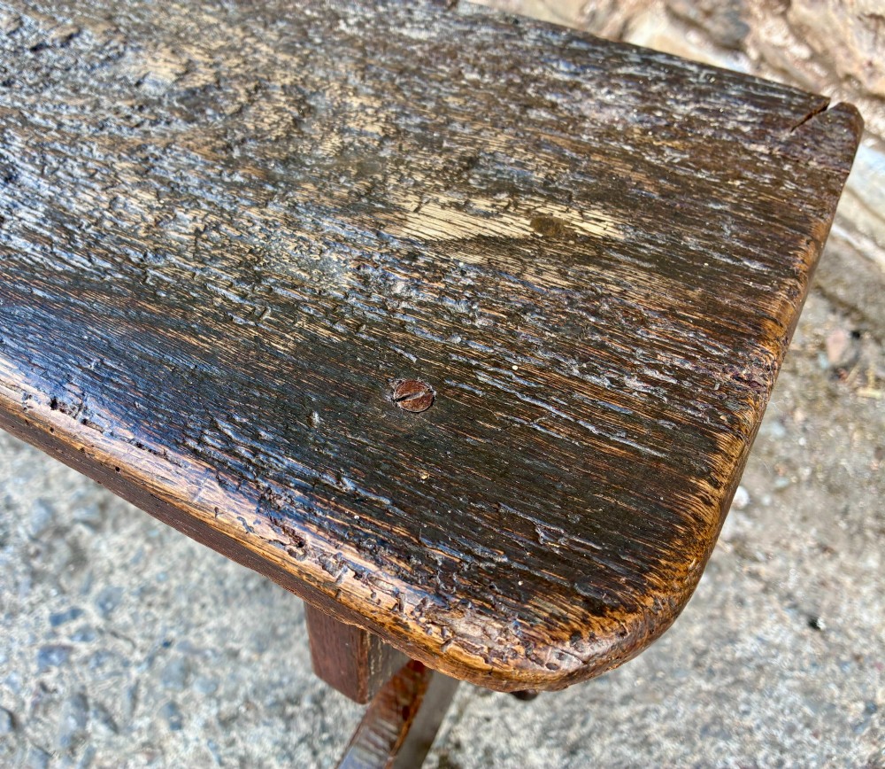 A long antique dark wooden hall bench featuring a flat plank seat, shaped slab end supports, and a lower wooden stretcher. View XII