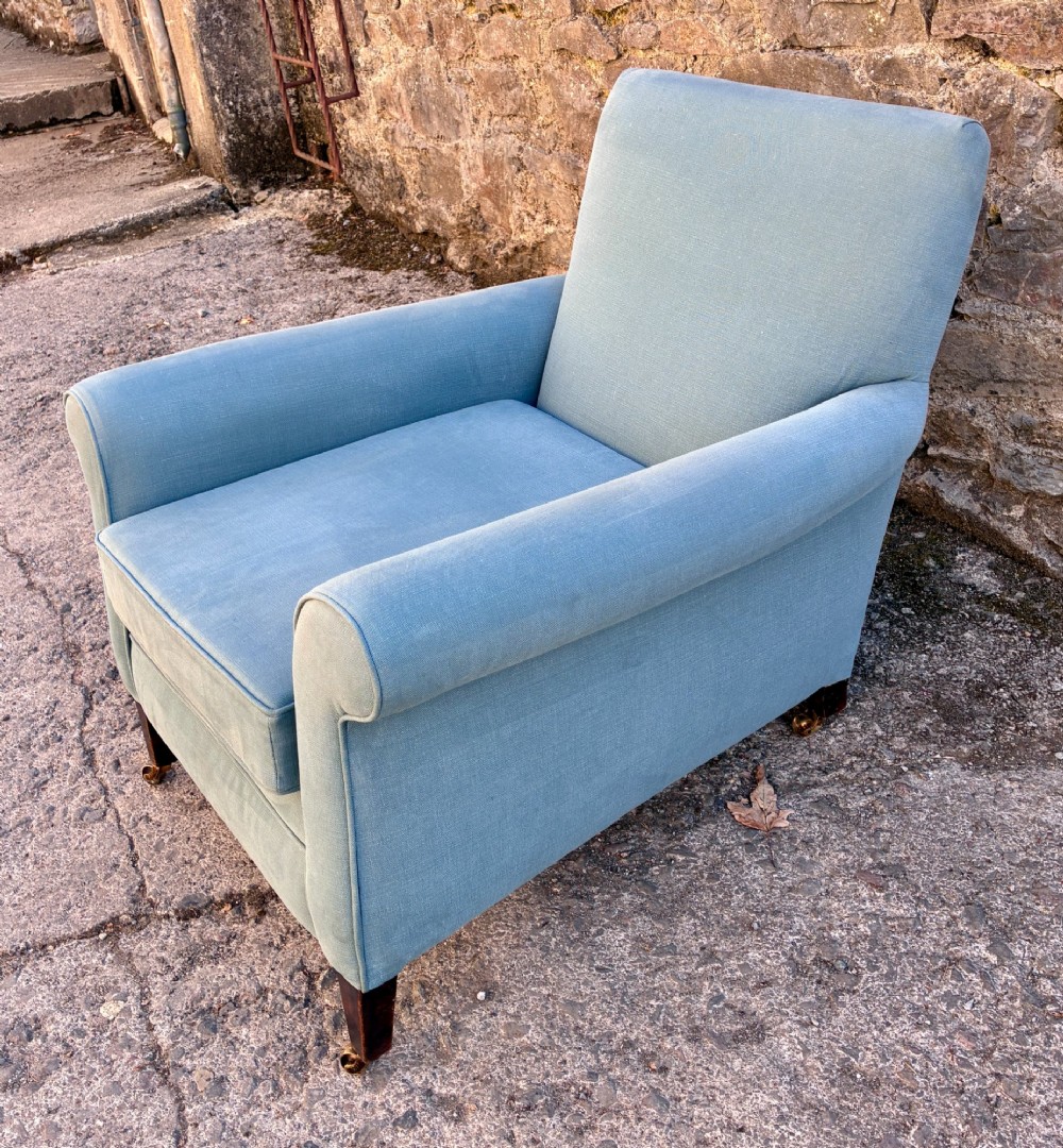An Edwardian deep-seated armchair upholstered in light blue woven fabric with scrolled arms and dark wood legs on brass castors. View II