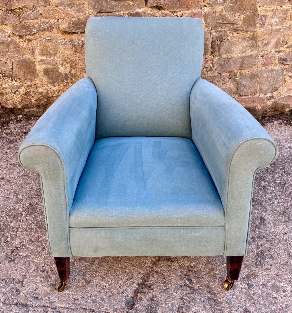 An Edwardian deep-seated armchair upholstered in light blue woven fabric with scrolled arms and dark wood legs on brass castors. View VII