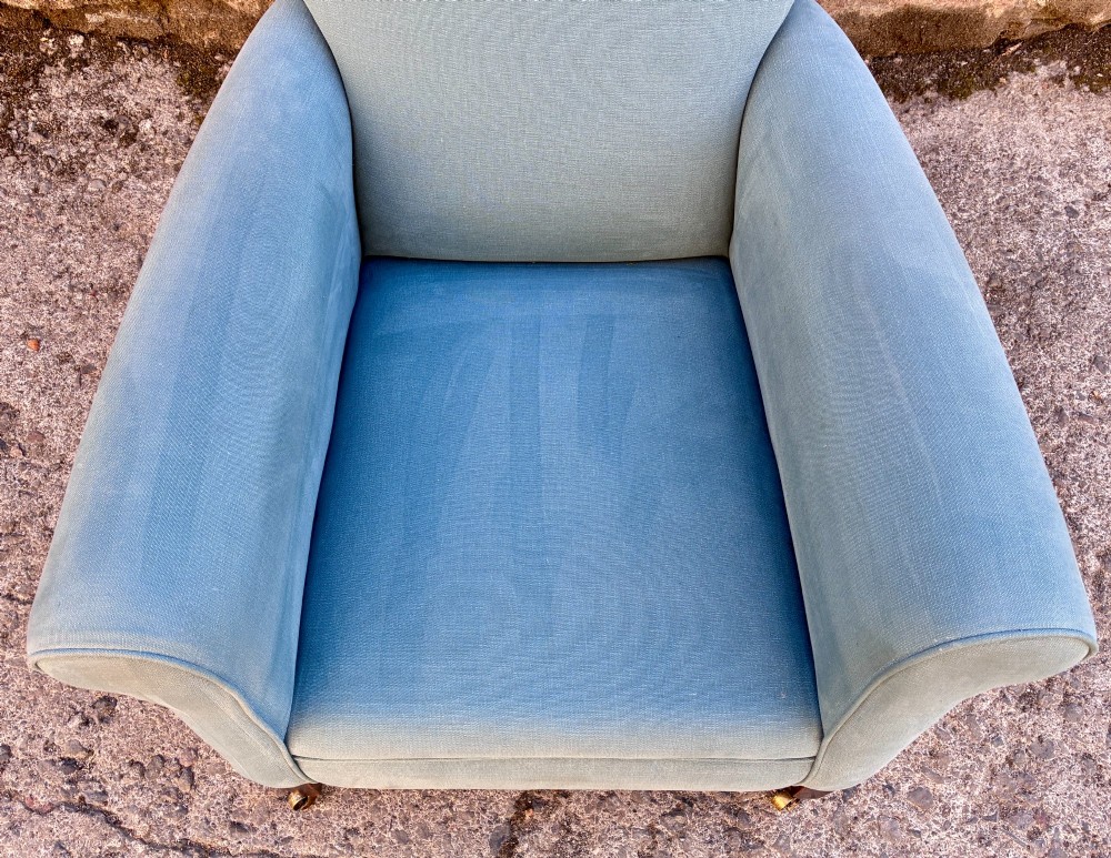 An Edwardian deep-seated armchair upholstered in light blue woven fabric with scrolled arms and dark wood legs on brass castors. View VIII