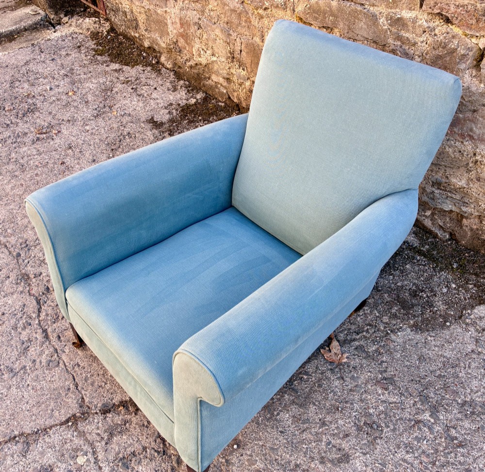 An Edwardian deep-seated armchair upholstered in light blue woven fabric with scrolled arms and dark wood legs on brass castors. View IX