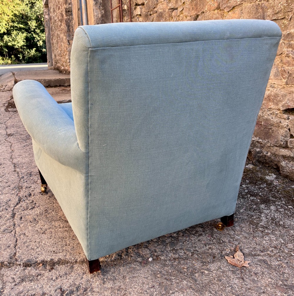 An Edwardian deep-seated armchair upholstered in light blue woven fabric with scrolled arms and dark wood legs on brass castors. View XI