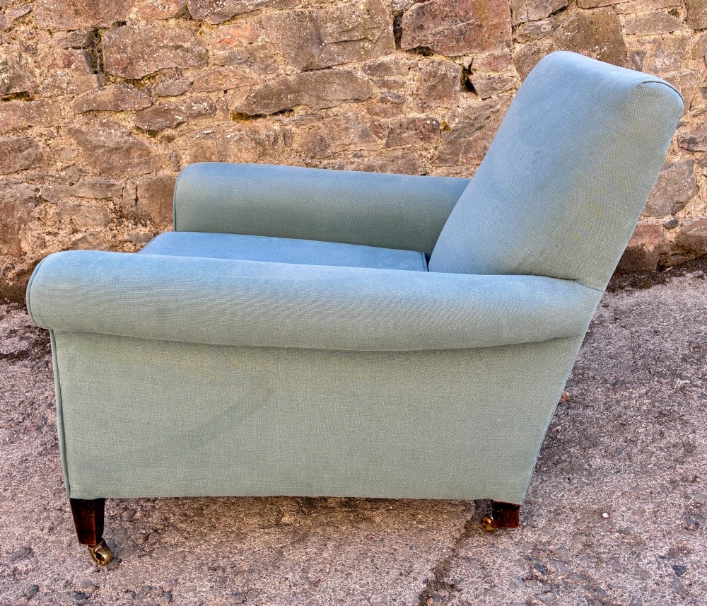 An Edwardian deep-seated armchair upholstered in light blue woven fabric with scrolled arms and dark wood legs on brass castors. View XII