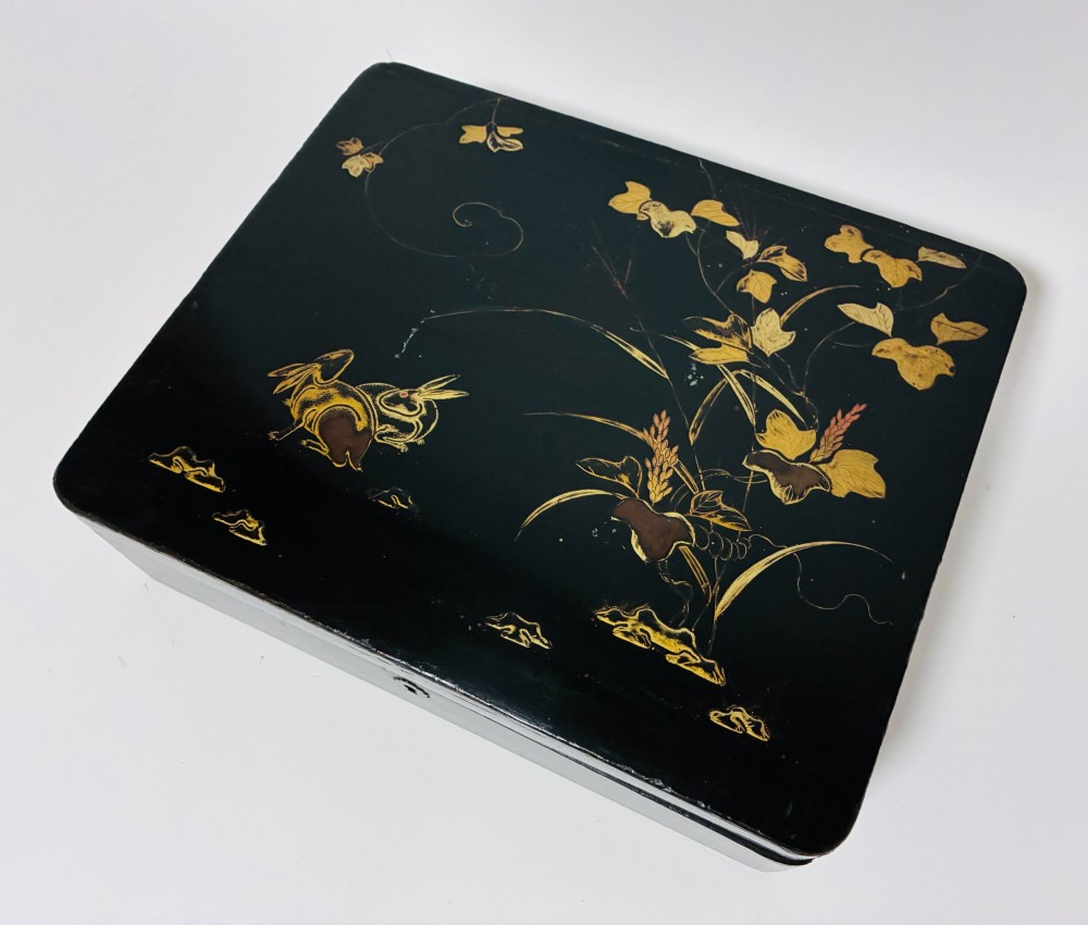 A rectangular black lacquered box decorated with gold maki-e depictions of rabbits and foliage, featuring a central metal keyhole. View II