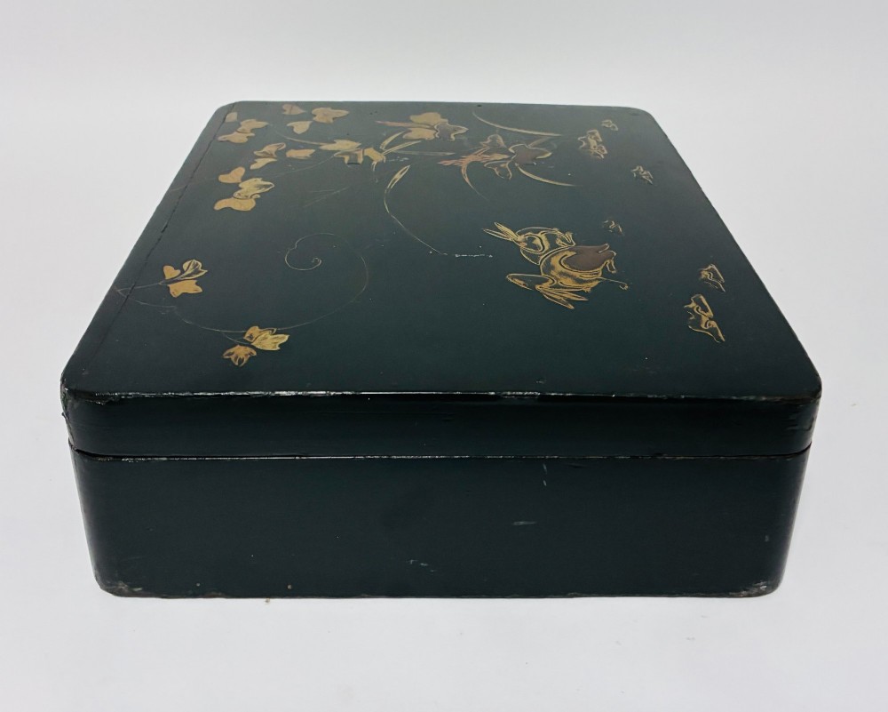 A rectangular black lacquered box decorated with gold maki-e depictions of rabbits and foliage, featuring a central metal keyhole. View IX