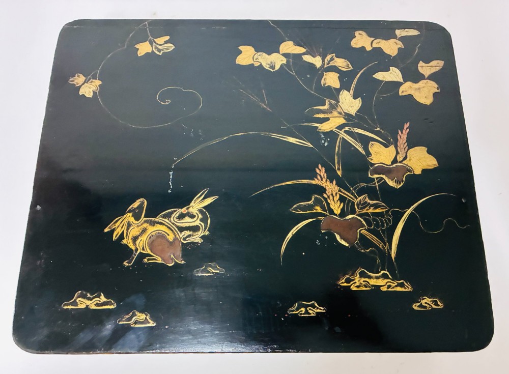 A rectangular black lacquered box decorated with gold maki-e depictions of rabbits and foliage, featuring a central metal keyhole. View XII